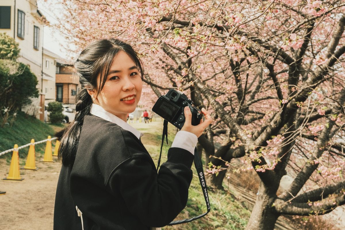 桜の木の下でカメラを手に微笑む早瀬 ちひろ
