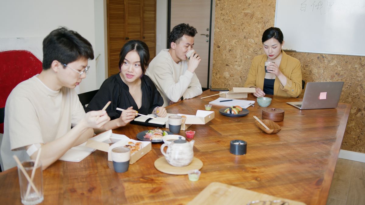 オフィスのテーブルを囲んでランチをとる社員たち